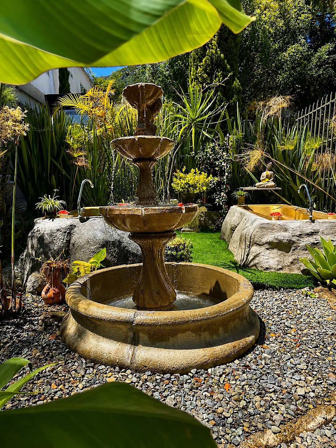 Jardín de Garden SPA con una fuente de piedra de tres niveles entre plantas y senderos de grava